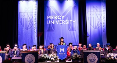 Student speaker at Commencement stage surrounded by faculty